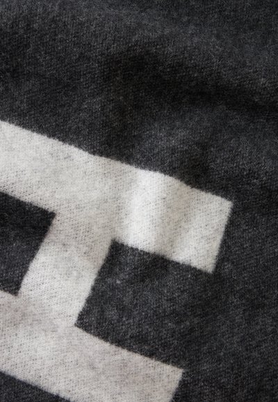 Gros plan d'un tissu doux et texturé avec un grand motif géométrique blanc sur fond gris foncé.
