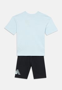 Lysblå kortærmet skjorte parret med sorte shorts, der har et lysblåt stiliseret bogstav "A" på venstre ben.