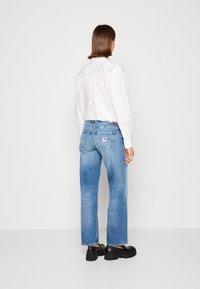 Světle modré džíny se rovnými nohavicemi, s vybledlým efektem a zadními kapsami. Nosič má na sobě bílou košili na knoflíky a černé platformové boty.