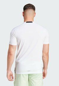 White short-sleeve athletic shirt with a black accent on the neckline, made of breathable fabric, featuring a small logo at the back hem.