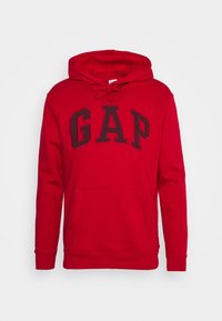 Sudadera roja fabricada con una mezcla de algodón, que presenta un gran logo negro de "GAP" en el frente, un bolsillo tipo canguro y una capucha ajustable con cordón.