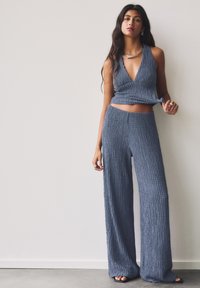 Blaues geripptes Strick-Zweiteiler-Set mit einem tiefen V-Ausschnitt und weiten Hosen, versehen mit einer strukturierten Oberfläche und verkürzten Design-Details.