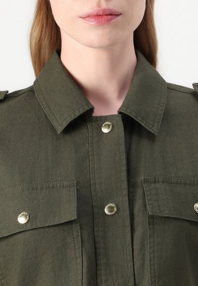 Chemise vert olive avec un design à col, dotée de deux poches poitrine, de boutons-pression argentés et d'épaulières pour un détail supplémentaire.