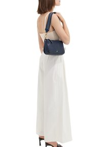 Navyblaues Lederhandtasche mit einem strukturierten Tragegurt, der blaue und gelbe Streifen aufweist, runder Form und goldenen Hardware-Akzenten.