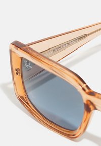 Óculos de sol transparentes castanhos com formato quadrado, feitos de material bio-baseado. Apresentam lentes cinzentas e um design de armação transparente.