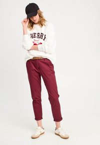 Hvid sweater med "Cherry" grafik, bordeaux cropped bukser, et flettet bælte og sort kasket, parret med beige sneakers med brune såler.