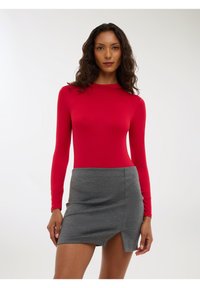 Body rosso a maniche lunghe abbinato a una mini gonna grigia con uno spacco laterale. Il body ha un design aderente e una texture liscia.