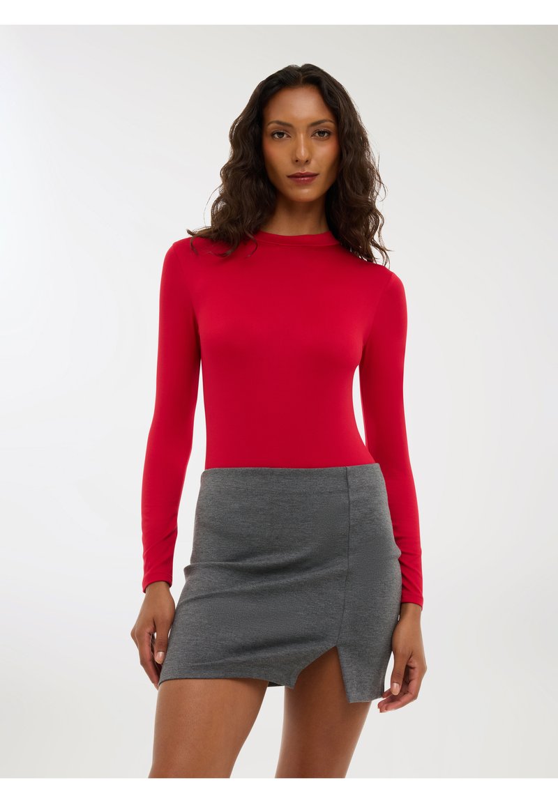 Body rosso a maniche lunghe abbinato a una mini gonna grigia con uno spacco laterale. Il body ha un design aderente e una texture liscia.