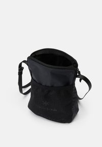 Borsa a tracolla nera in tessuto con chiusura a zip, una tasca in rete nella parte inferiore e una tracolla regolabile. Texture liscia e design semplice.