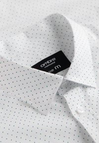 Camisa blanca de botones con pequeños puntos azules y verdes, de material de algodón, cuello clásico y etiqueta que indica la talla M.