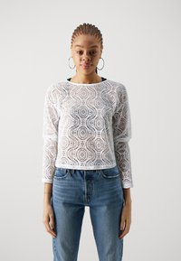Hvit blonde langermet topp med bølgemønster og rund hals, kombinert med høyt midje blå denimbukser.