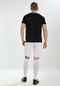 Black athletic jersey with short sleeves, paired with white shorts and knee-high white socks. Black soccer cleats are worn.