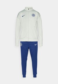 Nike træningsdragt i lys grå og blå. Jakken har højt krave og logo; bukserne har manchetter og logo. Lavet af glat, let stof.