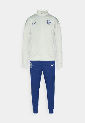 Chándal Nike en gris claro y azul. La chaqueta cuenta con un cuello alto y un logo; pantalones con puños y logo. Fabricado con un tejido suave y ligero.
