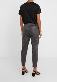 Grijze leren broek met een tapering fit en een elastische tailleband, gecombineerd met een aansluitend zwart t-shirt en zwarte sandalen met banden.