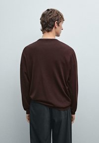 Maglione marrone a maniche lunghe realizzato in tessuto morbido con una vestibilità comoda. Design a girocollo visibile dal retro, abbinato a pantaloni scuri.