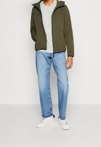 Oliivinvihreä huppari, vetoketjulla; vaaleanharmaa paita alla, siniset rentosomisteiset farkut, valkoiset lenkkarit.