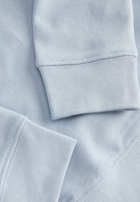 Ύφασμα φούτερ σε ανοιχτό μπλε χρώμα με ριπ μανσέτες, λεία υφή και ορατές ραφές κατά μήκος των ενώσεων.