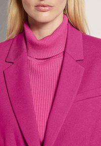 Fuchsia blazer with sharp lapels layered over a ribbed, fitted turtleneck in matching fuchsia hue, showcasing smooth texture and tailored design.