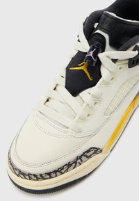Zapatilla blanca de cuero con acentos negros y amarillos, que presenta un diseño de estampado de elefante gris y una lengüeta negra texturizada, con cordones redondos.