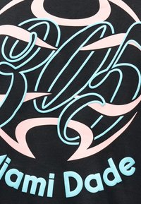 Design circulaire stylisé avec des lettres cursives bleu clair sur des formes rose pâle sur fond noir, texte « Miami Dade » sous le design.