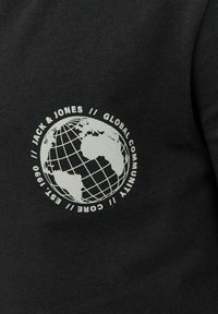 Svart bomullstyg med en vit globgrafik och texten: "JACK & JONES // GLOBAL COMMUNITY // CORE // EST. 1990." Prägling.