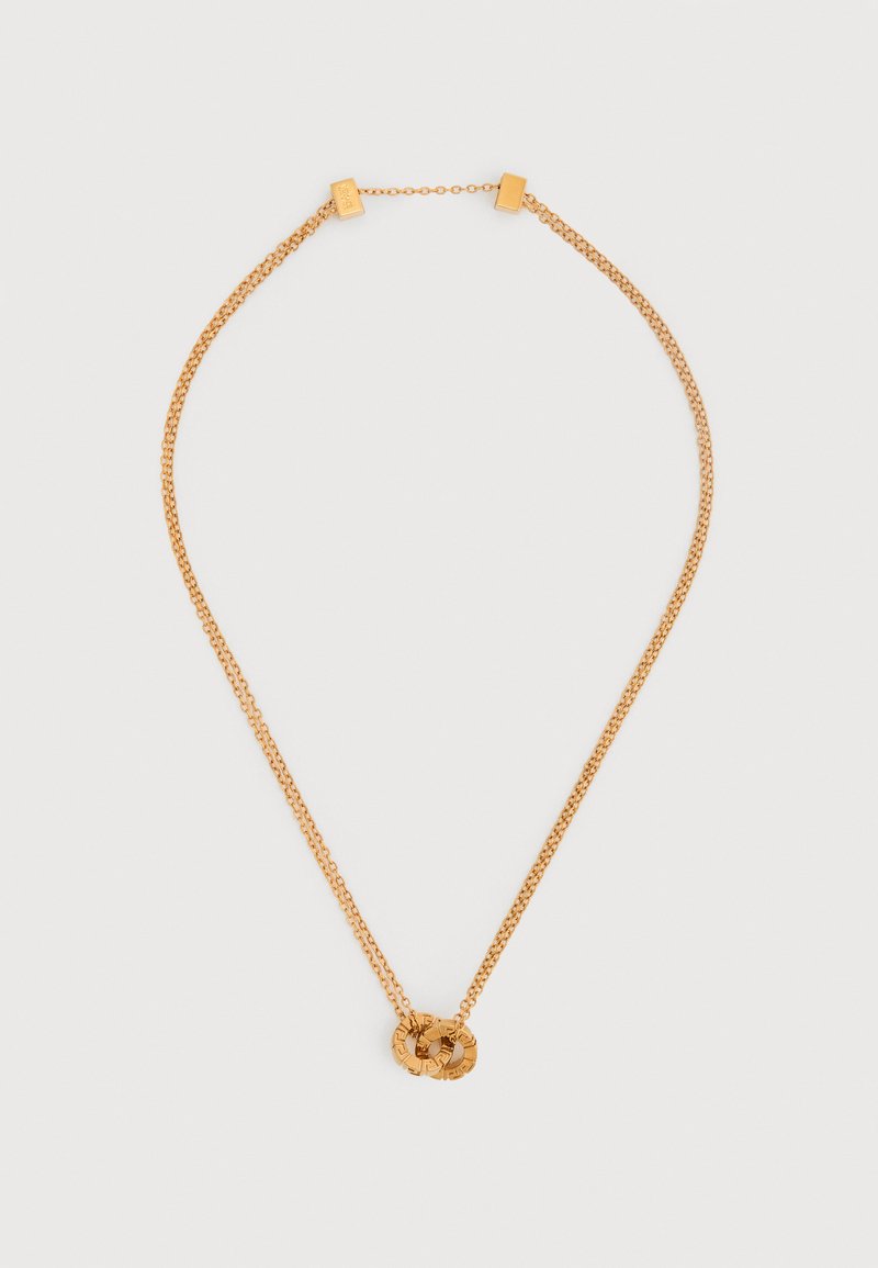 Χρυσό κολιέ με δύο διακοσμητικούς  κρίκους που επικάθονται ο ένας στον άλλο ως μενταγιόν, σε λευκό φόντο.