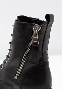 Bottine en cuir noir avec lacets à l'avant, fermeture éclair latérale et finition texturée. Le matériel couleur argent met en valeur le design.