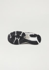 Semelle de chaussure de sport avec un motif en caoutchouc noir, des accents blancs et une forme courbée pour une meilleure adhérence et flexibilité.