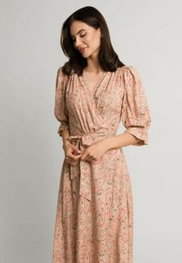 Maxi sukienka w kwiatowy deseń paisley, z delikatnymi odcieniami różu, dekoltem w serek oraz talią ściągniętą sznurkiem. Bufiaste rękawy dodają objętości.