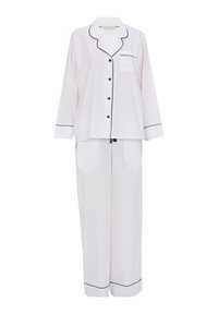 Witte zijden pyjama set met zwarte piping. Het shirt heeft een zak en knopen, terwijl de broek een losse, rechte pasvorm heeft.