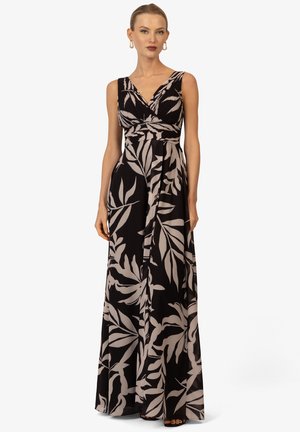 Maxikleid aus schwarzem Chiffon mit einem V-Ausschnitt, ausgestattet mit einem weißen Blättermuster, tailliertem Oberteil und fließendem Rock. Einfache schwarze Sandalen sichtbar.