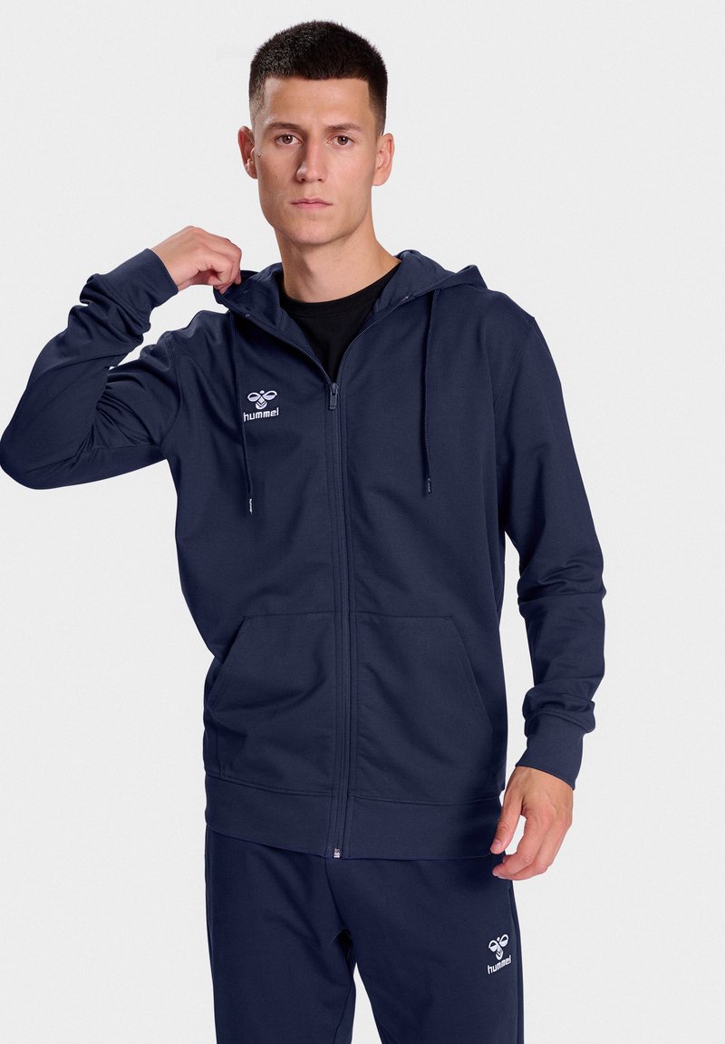 Marine blauwe rits hoodie gemaakt van zachte stof, met een kangoeroezak, verstelbare trekkoordkap en logo op de linkerborst.