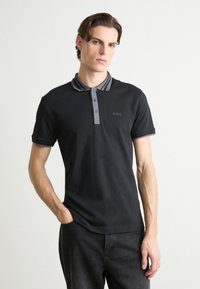 Svart polo shirt med grå randig krage, tre-knappslukning och en diskret 'BOSS'-logotyp på bröstet. Smoother tyg med korta ärmar.