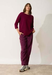 Pull en tricot bordeaux avec un col large, coupe décontractée. Associé à un pantalon en velours côtelé texturé de couleur assortie et à des baskets grises.