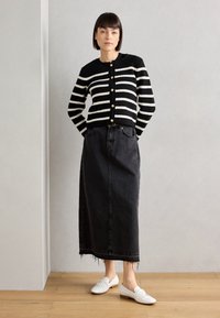 Black and white striped cardigan with gold buttons, paired with a long black denim skirt featuring frayed hem, and white loafers.