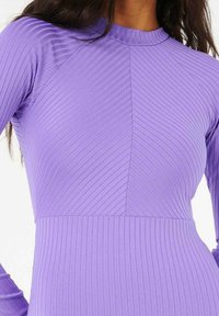 Robe en rib d'un violet profond à manches longues, présentant un col haut et des motifs texturés diagonaux sur l'ensemble du buste.