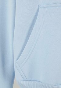 Tissu de sweat-shirt bleu clair montrant un gros plan d'une poche avant avec des coutures visibles et un ourlet côtelé.