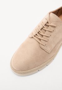 Scarpa in suede beige con design a lacci, punta rotonda e suola texturizzata. Caratterizzata da una superficie liscia e dettagli di cucitura minimi.