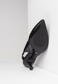 Scarpa nera con tacco alto, punta affusolata e superficie in vernice lucida e raffinata. Presenta una sottile cinturino alla caviglia e un tacco appuntito.