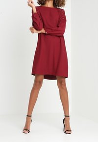 Robe bordeaux à manches longues avec une coupe décontractée, ornée de détails embellis aux épaules et d'un col arrondi, fabriquée en tissu doux.