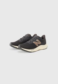 Une paire de chaussures de course en mesh noires avec des semelles rembourrées beiges et un logo "N" en imprimé léopard sur les côtés, posées sur un fond clair uni.