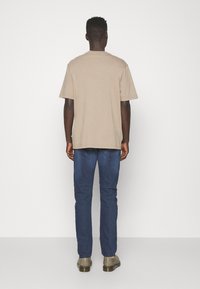 Beige cotton t-shirt with a relaxed fit, short sleeves, and a crew neck. Paired with dark blue denim jeans and gray boots.