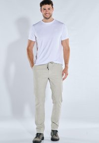 Lässiges Outfit mit einem weißen Baumwoll-T-Shirt und beigen Jogginghosen mit Kordelzug, ergänzt durch graue Wanderschuhe. Einfaches Design und entspannter Schnitt.