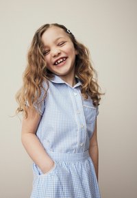 Robe vichy bleue et blanche à manches courtes, devant à boutons, col et poche. Présente une taille froncée avec une texture douce.