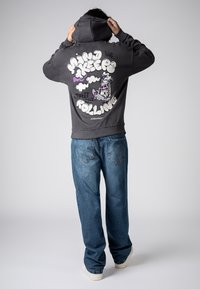 Donkergrijze hoodie met een grafische afbeelding op de achterkant van cartoontekst en een figuur. Gecombineerd met blauw, losvallende spijkerbroeken en witte sneakers.