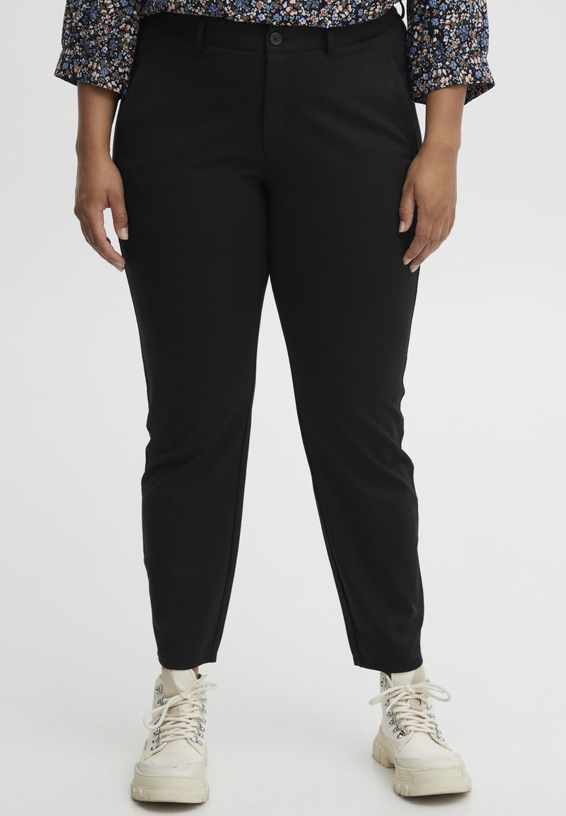Svarta skräddarsydda byxor har en slim fit, slät textur och knappstängning. Bärs med vita sneakers, vilket ger en avslappnad look.
