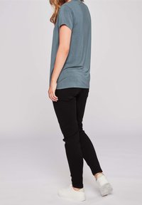 Modré tričko s krátkým rukávem a volným střihem, kombinované s černými slim-fit džíny a bílými teniskami. Hladká tkanina a jednoduchý design.