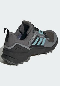 Schwarzer und grauer Trailschuh mit strukturiertem Obermaterial, hellblauen Akzenten, verstärktem Fersenbereich und Gummisohle mit Profilstollen.