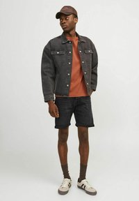 Donkerdenim jacket met voorzakken, roestkleurig t-shirt, zwarte denim shorts, bruine sokken en crèmekleurige sneakers met zwarte strepen.